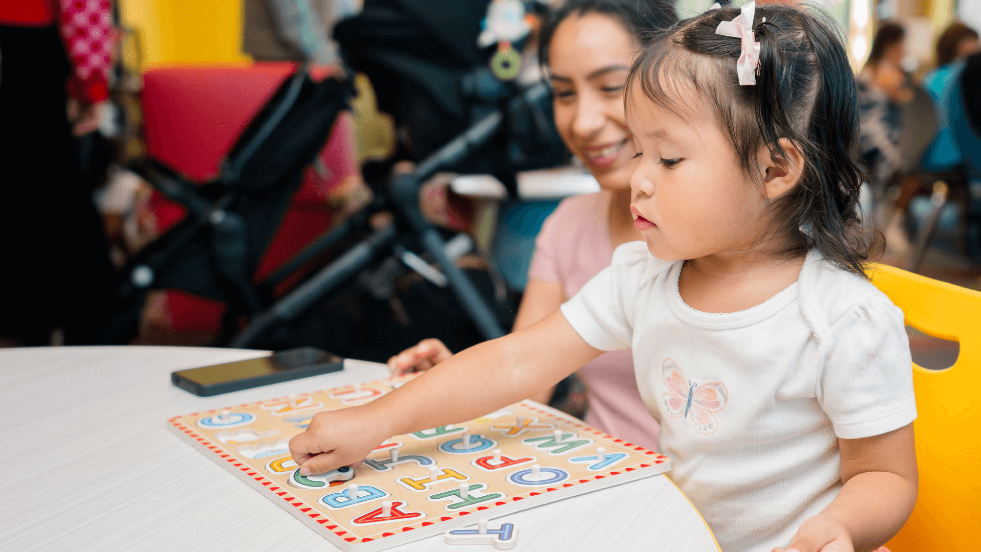 Child placing wooden letter pieces into a puzzle at a library table.